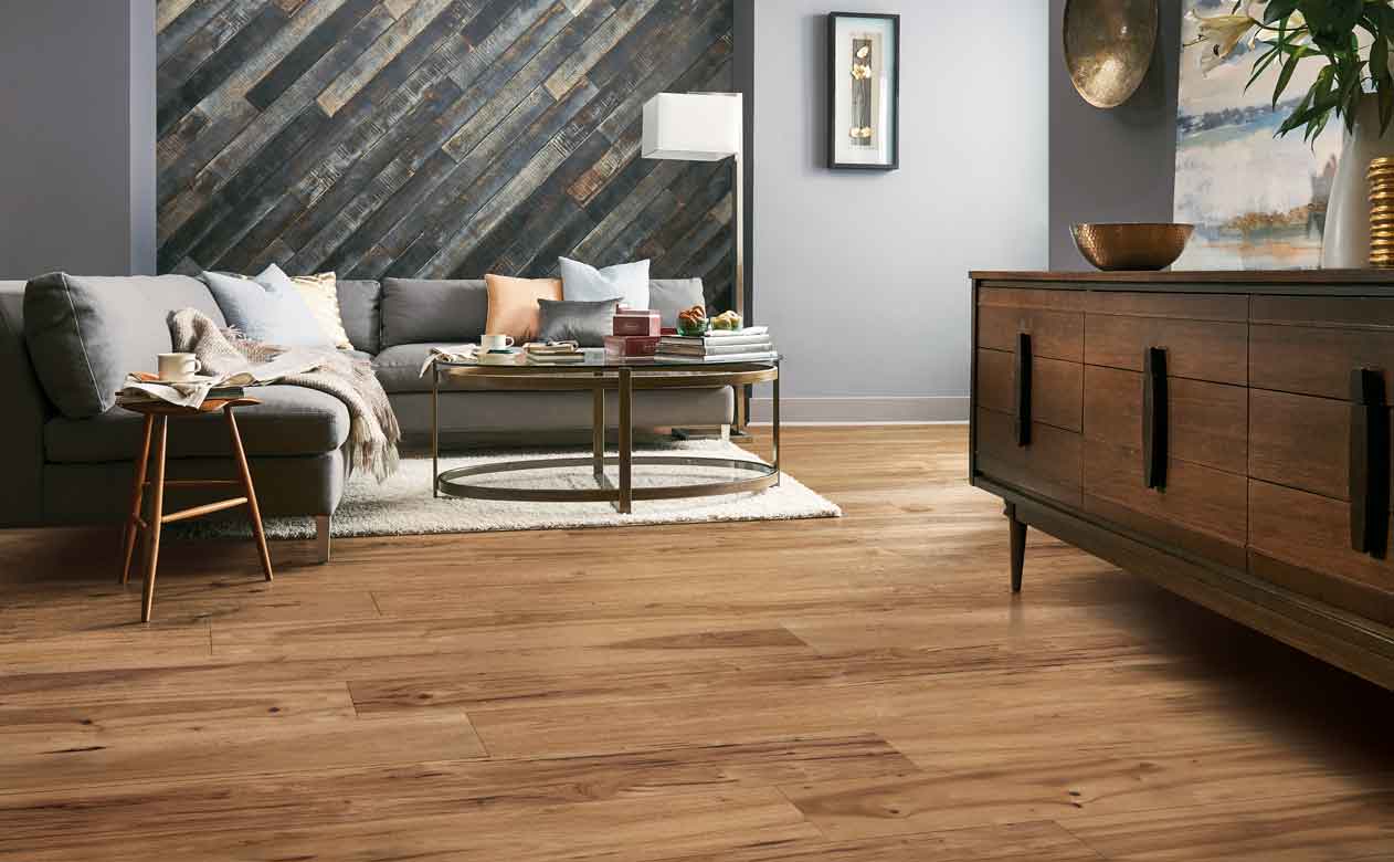 honey hued hardwood in modern living room with gray wood accent wall, gray couch, and sideboard